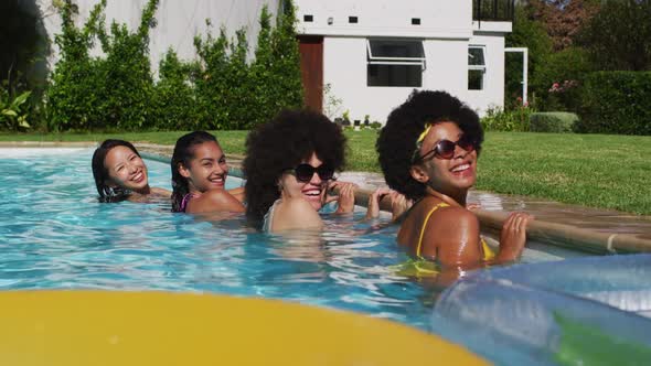 Diverse group of female friends standing at the poolside looking at the camera alt