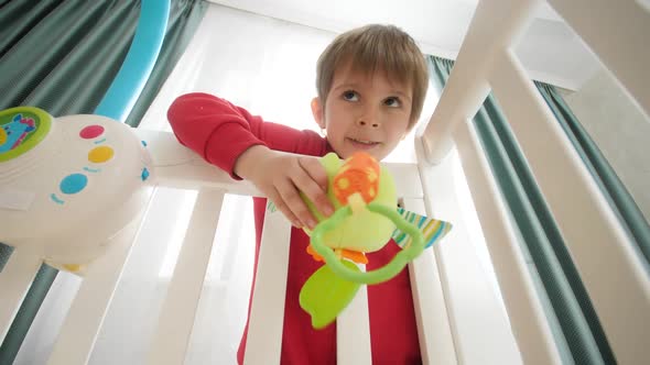 Cute Little Boy Playing Toys with His Little Baby Brother Lying in Crib alt