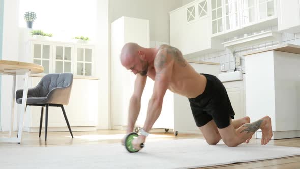 Muscular Man in Shorts Doing Exercises with an Abs Wheel in Living Room at Home