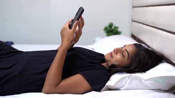 Attractive and beautiful Indian young women smiling while using phone on bed alt
