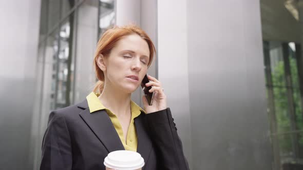 Businesswoman in city using smart phone with takeaway coffee