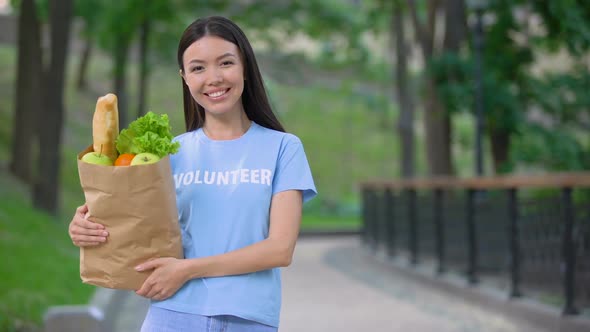 Cheerful Female Volunteer Holding Grocery Bag Outdoors Smiling Camera, Donation alt
