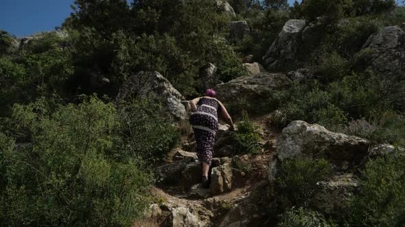 A Girl in a Long Dress Climbs a Stone Rock on a Sunny Day