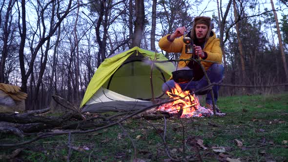 The Guy Prepares Food Near a Campfire and a Tent in the Woods alt