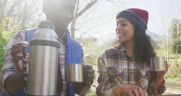 Smiling diverse couple drinking tea and hiking in countryside alt