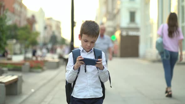 a Schoolboy Simultaneously Walks Along a City Street and Plays Modern Games on a Gadget