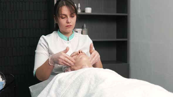 Cosmetologist Woman Hands Makes a Facial Massage to a Young Man in a Salon