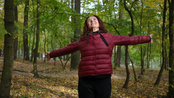 Portrait of Happy Mature Woman Stretching Hands Spinning Looking Up Standing in Autumn Forest alt