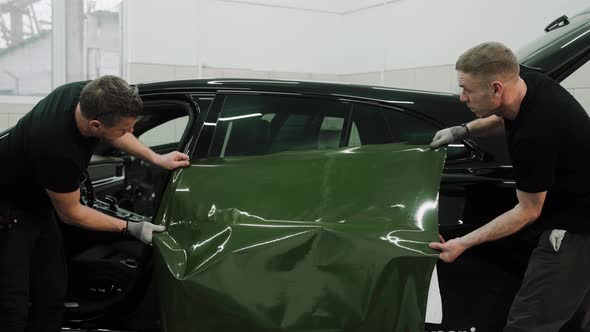 Two Men are Vinyl Wrapping a Car in Khaki Green Color Applying Wrap to the Door