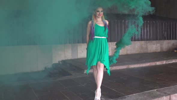 Cute Girl in a Green Dress with African Braids and Colorful Makeup Posing with Bright Green Smoke on alt