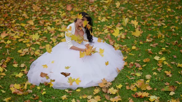 Beautiful Bride in Autumn Day Sitting on Grass with Yellow Maple Leaves Happy Woman alt