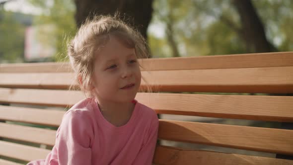 Pretty Happy Girl Sits on Wooden Bench in Sunny Park Closeup alt