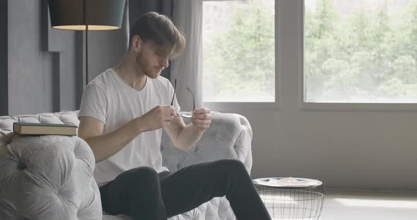 Young Bearded Man Entering Room, Putting on Eyeglasses and Opening Book alt