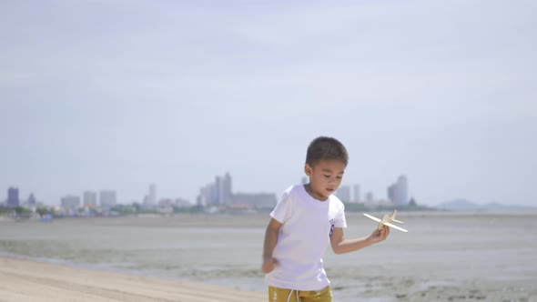 Happy little child boy playing with toy airplane flights at tropical beach alt