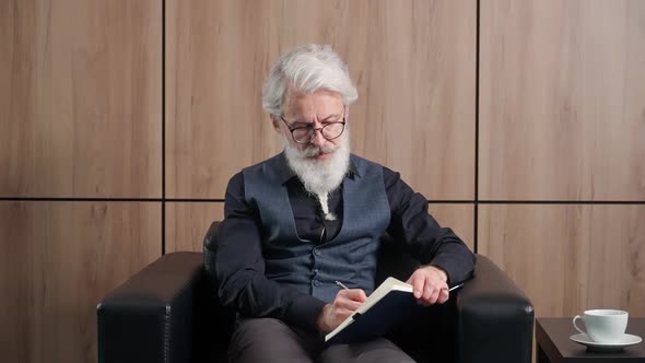 Grayhaired Man Works in the Office Art Director Writes Down Ideas and Concepts in a Notebook an alt