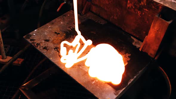Glassblower pouring molten glass on metal work bench alt