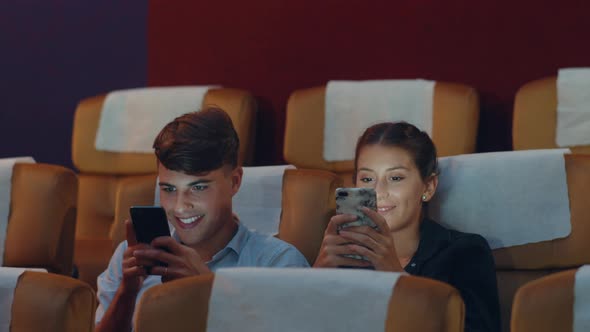young caucasian couple using smartphone while watching film in movie theater.