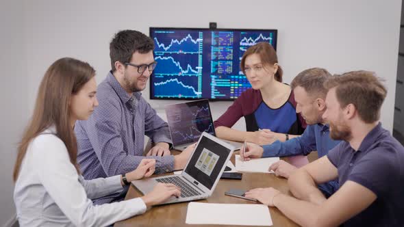 Group of Young Financial Specialists Is Sitting in Meeting Room with Display with Schedules on Wall alt