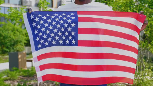 Close Up Afroamerican Man Holding American Flag on Background Trees in Summer alt