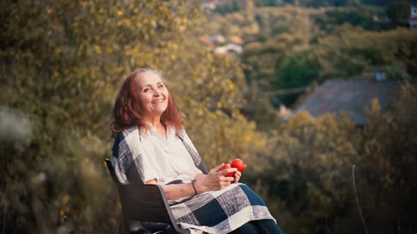 A Mature Adult Woman Dreamily Sits with Apples in Her Hands alt