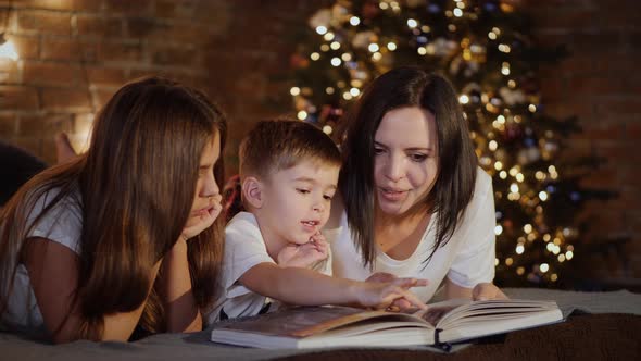 Mom with Children Lying on the Bed Reading a Book Together alt