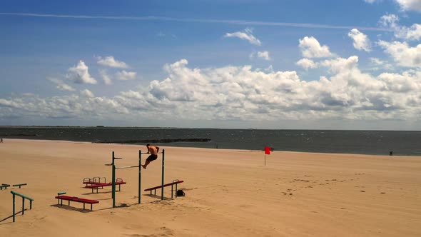 drone camera steady shot, as a young man exercises on a pull up bar on Coney Island beach in Brookly alt