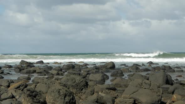 Ocean waves crashing and breaking on a high wind day. Large black rocks lay on the coastal foreshore alt
