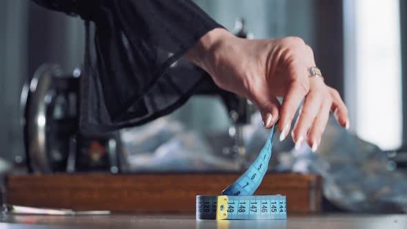 Seamstress is taking up blue tape measure on the background of sewing machine alt