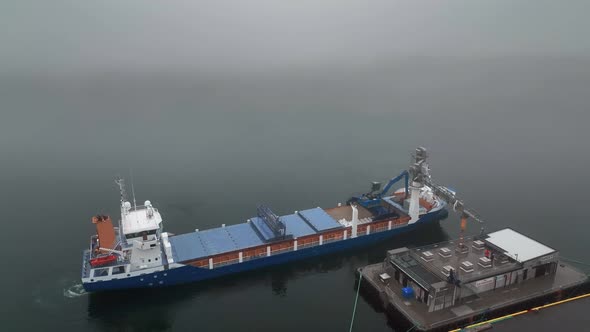 Bulk Carrier Unloading Dry Cargo At The Port Of Faskrudsfjordur On A Foggy Day In East Iceland. aeri alt