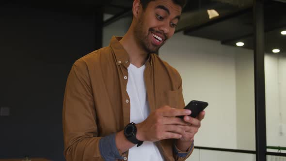 Mixed race businessman standing using a smartphone in a modern office alt