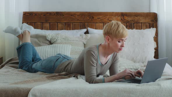 Focused Attractive Woman Lying in Comfortable Bed Typing on Notebook Computer Browsing Internet alt