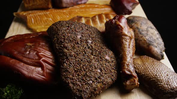 Rotating shot of a variety of delicious, premium smoked meats on a wooden cutting board alt