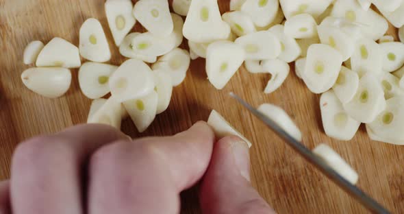 Male Hands Slicing Peeled Cloves of Garlic Into Pieces alt