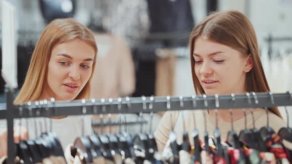 Women Friends Looking at Clothes on Hangers at Store alt
