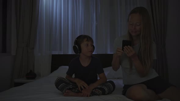 A Woman at Night Turns on a Meditation Relaxation Application on Her Phone for Her Son to Relax alt