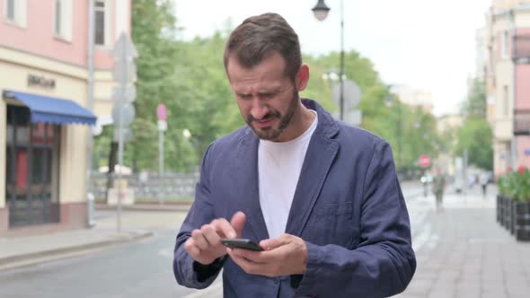 Man Reacting to Loss on Phone While Walking Down the Street alt