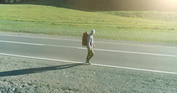 Flight Over Hitchhiker Tourist Walking on Asphalt Road. Huge Rural Valley at Summer Day. Backpack alt