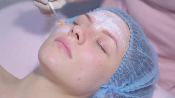 Cosmetologist Applying Face Moisturizing Mask on Young Woman's Face