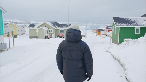 Man In Winter Coat Walking Through Snow Covered Street Of Ilulissat alt
