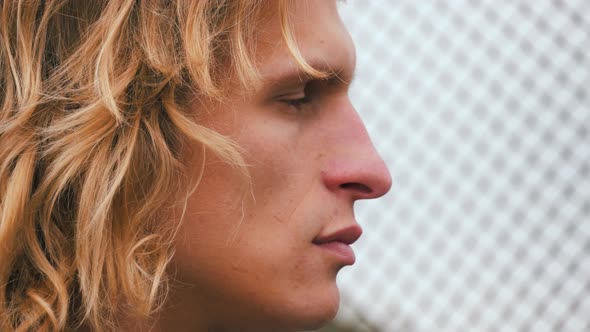 Close up shot of attractive young blond man with long hair. Wind plays with wavy hair.