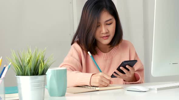 Young Asian women business owners using app smartphones and take notes in the office.