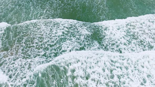Drone view into wave crashing to the sandy beach and foaming  surface turquoise blue clean water. alt