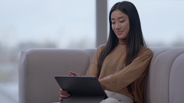 Portrait of Beautiful Confident Asian Woman Rejoicing Startup Success Scrolling Tablet in Home alt