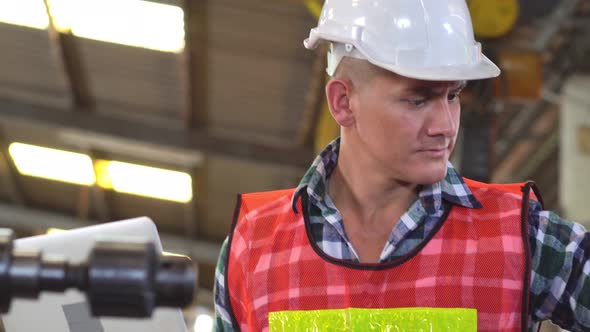 Male factory foreman using laptop checking on metal machine in the factory alt