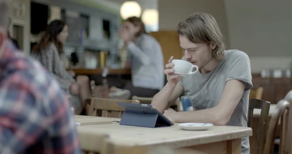 Man using digital tablet and drinking coffee while sitting in pub