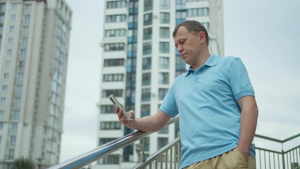 Portrait of a Man with a Mobile Phone in His Hands Stands on the Stairs Buildings Background