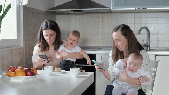 2 mothers with babies use the phone and do not look at each other. Friendly meeting, guests alt