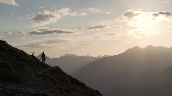 A girl in a dress walks on a path trough the mountains. You can only see her silhouette against the alt