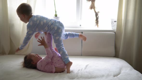 Two Smiling Preshool Toddler Children Boy and Girl Lieing on Back in Pajamas on White Bed alt