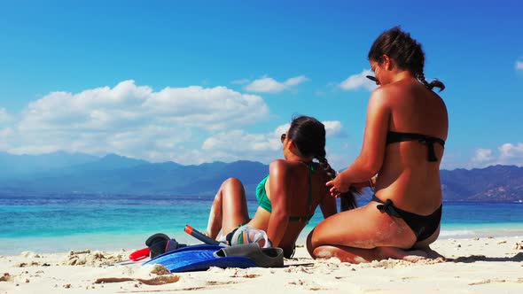 Girls in bikini who are friends, fixing hair while talking about vacations, sitting on exotic beach alt